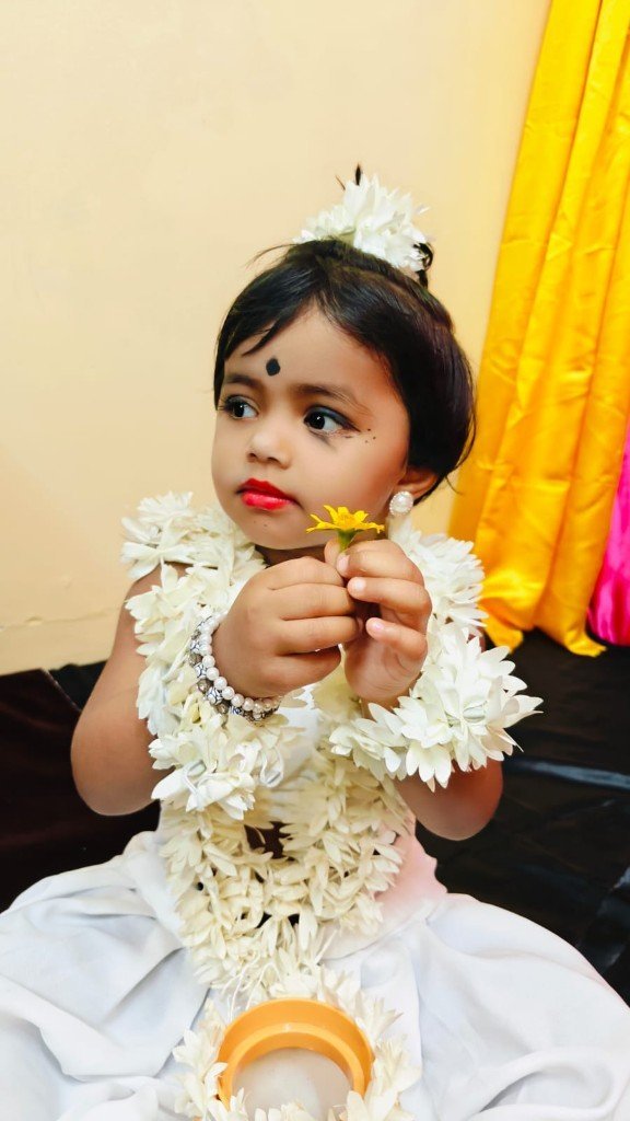 Toddler in traditional floral attire holding a yellow flower
